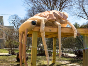 A life-sized Galerucella beetle made of brown and beige fabric.