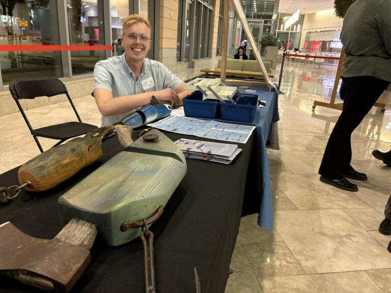 Blonde man poses next to large-format hand carved fishing lures