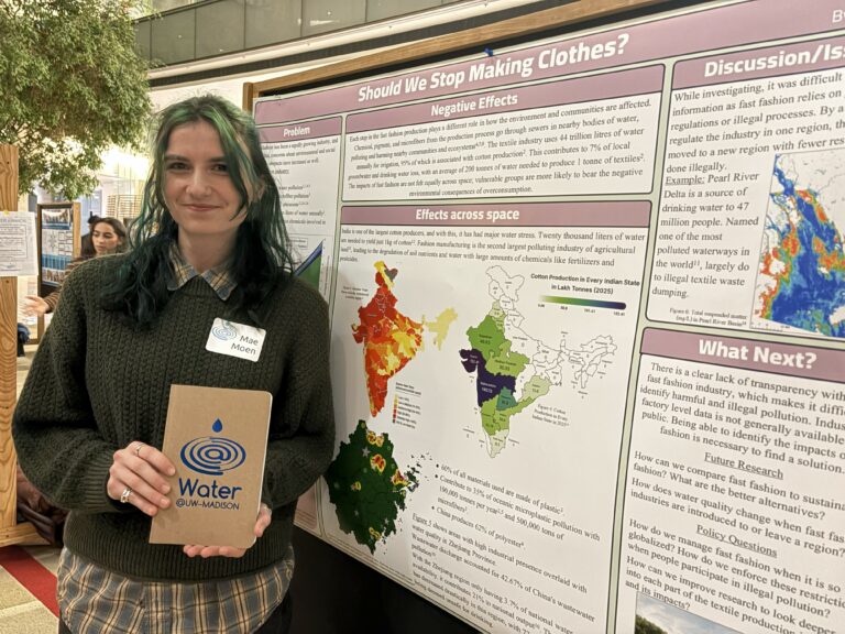 Woman with blue and brown hair stands next to a scientific poster