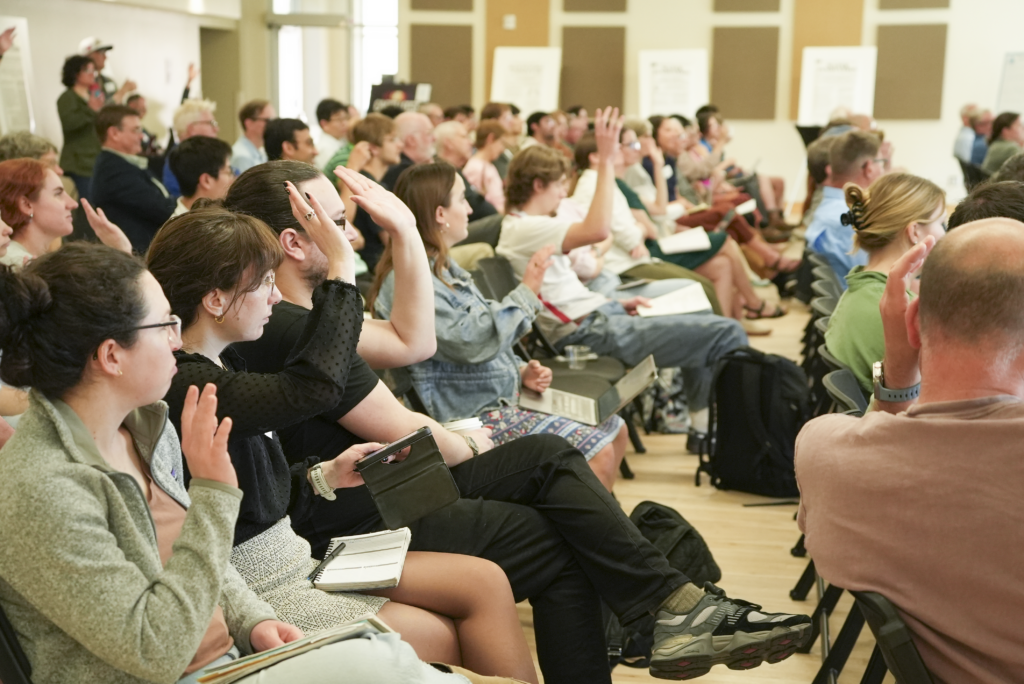 Image of event attendees at the 2026 Spring Symposium, raising hands