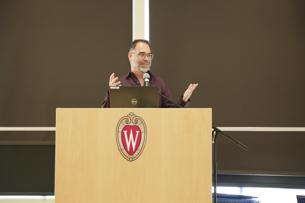 man speaks and gestures behind podium