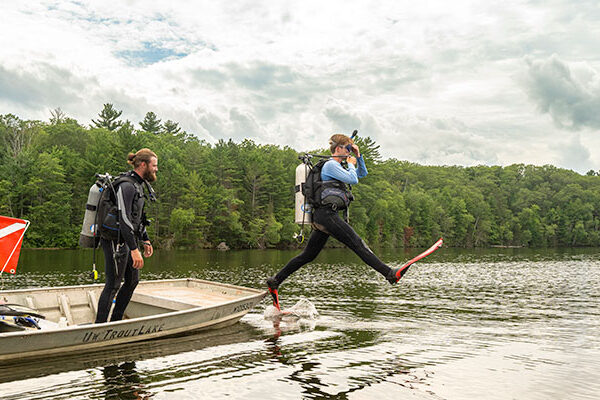 Scuba diver giant-stepping into a lake from a research jon boat.